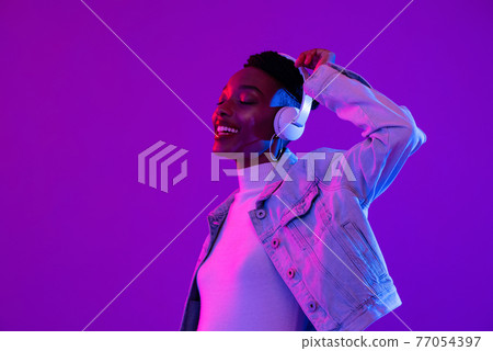 African American woman wearing headphones listening to music in futuristic purple cyberpunk neon 77054397
