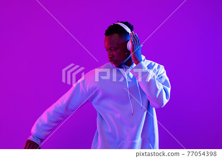 African man wearing headphones listening to music and dancing in futuristic purple cyberpunk neon African man wearing headphones listening to music and dancing in futuristic purple cyberpunk neon 77054398