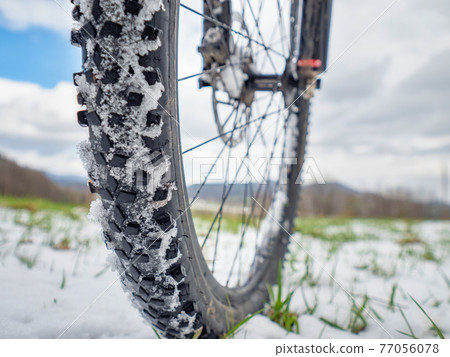Front wheel in the snow. Detailed extreme close up low angle view. Snowy filed in open landscape. Front wheel in the snow. Detailed extreme close up low angle view. Snowy filed in open landscape. 77056078