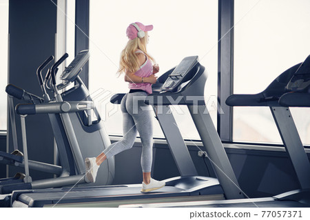 Side view of sporty blonde woman exercising on treadmill in gym 77057371