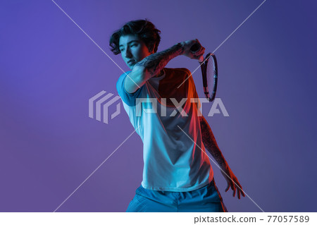 Young caucasian man playing tennis isolated on purple-blue studio background in neon, action and motion concept Young caucasian man playing tennis isolated on purple-blue studio background in neon, action and motion concept 77057589