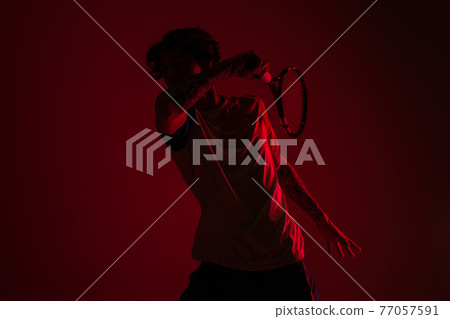 Young caucasian man playing tennis isolated on red studio background in neon, action and motion concept 77057591
