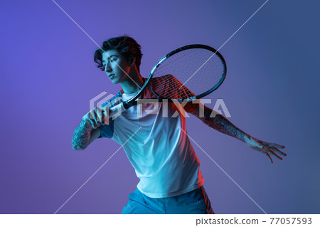 Young caucasian man playing tennis isolated on purple-blue studio background in neon, action and motion concept Young caucasian man playing tennis isolated on purple-blue studio background in neon, action and motion concept 77057593