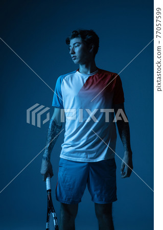 Young caucasian man playing tennis isolated on blue studio background in neon, action and motion concept 77057599