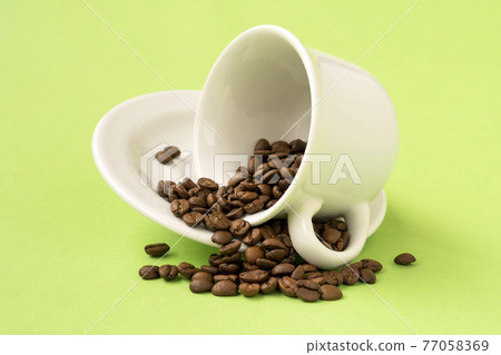 White cup with coffee beans falling on a green background White cup with coffee beans falling on a green background 77058369