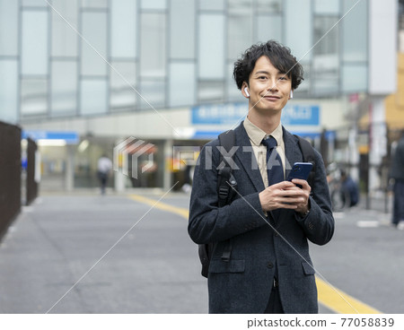 A man in his early 30s wearing headphones with a smartphone 77058839
