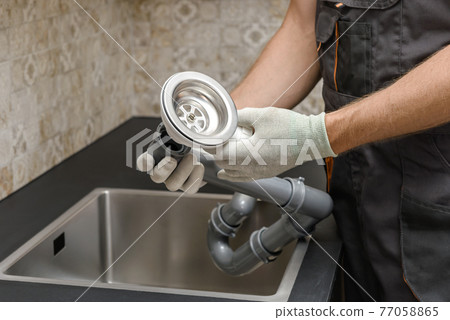 An worker is installing a sewer drain for the kitchen sink. 77058865