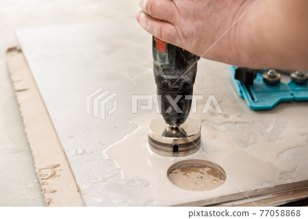 A tiler is using a diamond crown to drill holes in the ceramic tile. A tiler is using a diamond crown to drill holes in the ceramic tile. 77058868