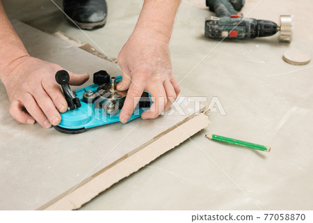 A tiler uses a caliper with a suction cup to drill holes in the ceramic tile. 77058870