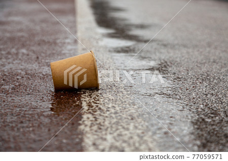 Kyiv, Ukraine - March, 22, 2020: Used paper cup on a wet road. 77059571