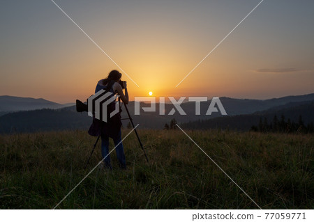 Photographer shoots landscape at sunset Photographer shoots landscape at sunset 77059771