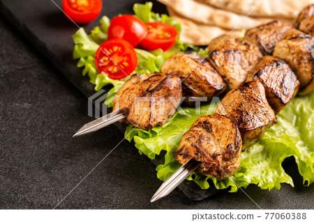 Two portions of shish kebab on a stone plate with salad. 77060388