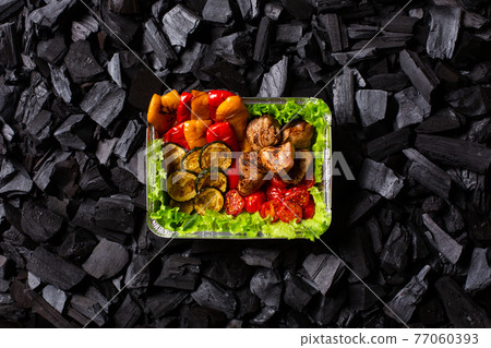 Ready shish kebab. Portion of grilled meat and vegetables in a disposable container on charcoal background. Copy space. Ready shish kebab. Portion of grilled meat and vegetables in a disposable container on charcoal background. Copy space. 77060393