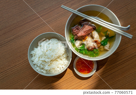 Top view Asian meal, a bowl of pig's blood soup and pork with steam white rice and spicy-sour sauce, natural light on table. Pig's blood soup and pork is called Tom Leard Moo in the Thailand language. 77060571