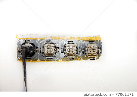 Electrical wire and opened plug socket on the old plastering wall.  77061171