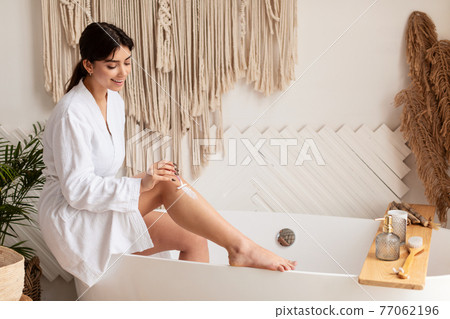 Woman Shaving Legs With Razor Sitting On Bathtub In Bathroom 77062196