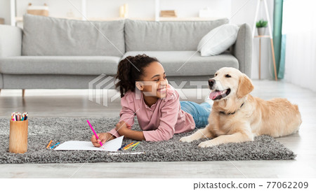 Young afro girl drawing with dog at home 77062209