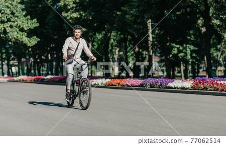 Cheerful young employee with helmet on utility bicycle rides to modern workplace Cheerful young employee with helmet on utility bicycle rides to modern workplace 77062514