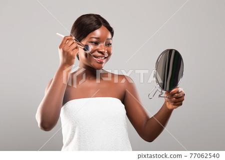 Happy Young Black Female Holding Makeup Brush And Looking Into Mirror Happy Young Black Female Holding Makeup Brush And Looking Into Mirror 77062540