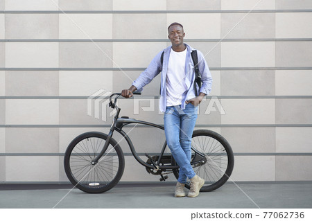 Full length portrait of happy black guy with modern bike standing on city street and looking at camera 77062736