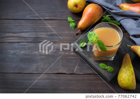 Natural pear juice in a glass cup. Juicy ripe conferences pears and mint leaves. top view copy space Dark rustic wooden background. 77062742