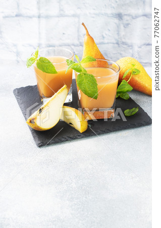 Natural pear juice in a glass cup. Juicy ripe conferences pears and mint leaves. copy space Slate stand, light concrete background. 77062747