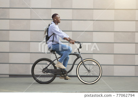 Side view of cool black guy with earphones racing on his bicycle near brick wall downtown 77062794