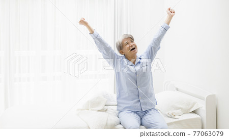 Senior man in pajamas that stretches with a smile 77063079