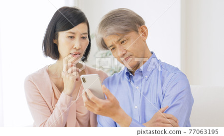 中年夫婦一邊看智能手機一邊思考 77063195