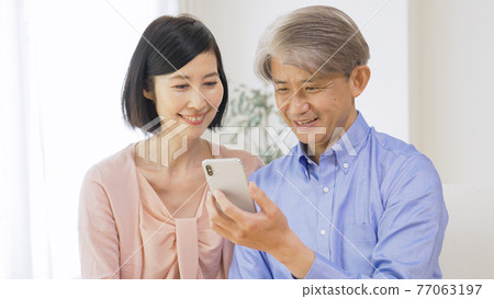 Middle-aged couple looking at a smartphone Middle-aged couple looking at a smartphone 77063197