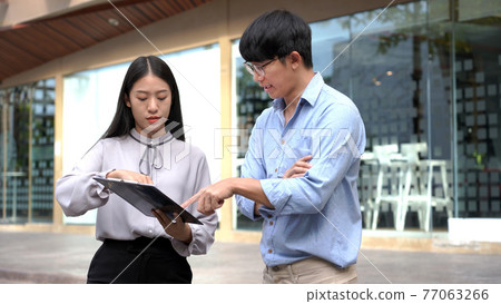 Business concept two coworkers helping each other to revise the contract before signing signature carefully in front of the office. 77063266