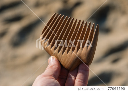 A hand holding natural wooden comb for scalp massage and aroma combing. Hair care concept. 77063590