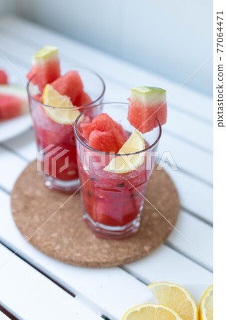 Fresh watermelon refreshing summer cocktail smoothie with lemon and ice in glass mug on white wooden board Fresh watermelon refreshing summer cocktail smoothie with lemon and ice in glass mug on white wooden board 77064471