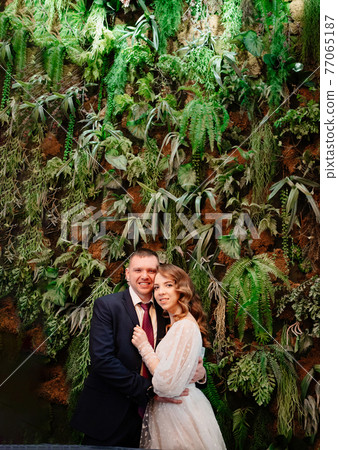 happy bride and groom at the wall decorated with live plants.  77065187