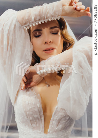 portrait of a bride and a white dress with long sleeves, hands near the face. portrait of a bride and a white dress with long sleeves, hands near the face. 77065188