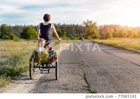 Young adult caucasian mom enjoy having leisure fun riding bicycle with cute adorable blond daughter holding wild field flower at scenic rural country road on bright sunny day. Countryside vacation 77065191