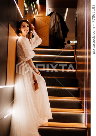 the bride in a white dress stand on poorly lit staircase 77065192