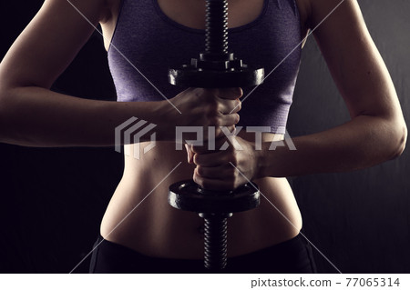 Slim athletic woman Holding dumbbell in the hand on black Slim athletic woman Holding dumbbell in the hand on black 77065314