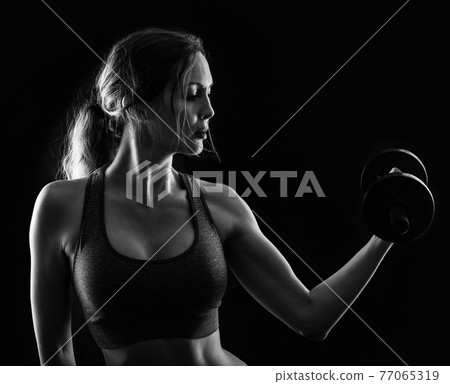 Slim athletic woman Holding dumbbell in the hand on black Slim athletic woman Holding dumbbell in the hand on black 77065319