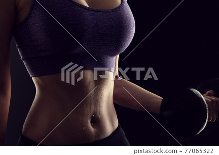 Slim athletic woman Holding dumbbell in the hand on black Slim athletic woman Holding dumbbell in the hand on black 77065322