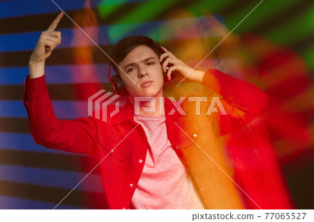 young man in red shirt with headphones listening to music 77065527