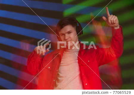 young man in red shirt with headphones listening to music young man in red shirt with headphones listening to music 77065529