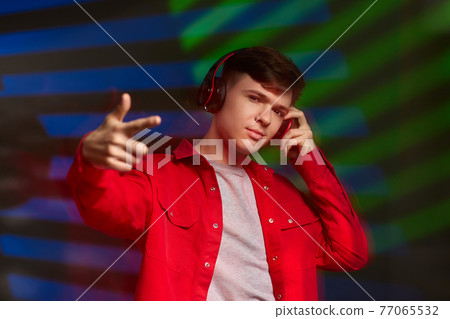 young man in red shirt with headphones listening to music 77065532