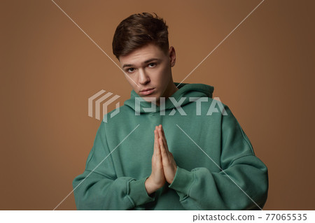 young guy in sweatshirt putting hands together as if he is praying young guy in sweatshirt putting hands together as if he is praying 77065535