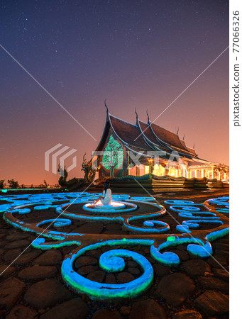Wat Sirindhorn Wararam Temple or Wat Phu Prao with Asian woman sitting on glowing sculpture and illuminated church in the night at Ubon Ratchathani 77066326