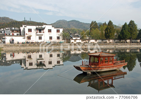 Xidi Ancient Town in Anhui Province, China. A house in the old town seen across Ming Jing Lake with boat. Ancient town of Xidi in China with old buildings, lake and trees in fall. Xidi Ancient Town in Anhui Province, China. A house in the old town seen across Ming Jing Lake with boat. Ancient town of Xidi in China with old buildings, lake and trees in fall. 77066706