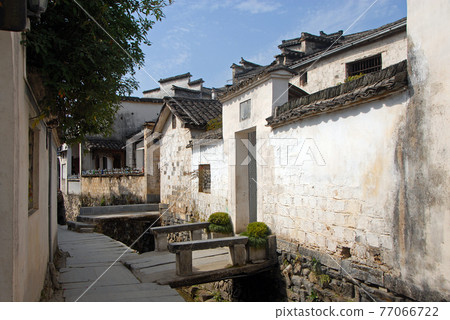 Xidi Ancient Town in Anhui Province, China. A quiet street in the old town of Xidi called the Back Rivulet. The path follows a stream past houses and a bar. Traditional architecture in Xidi, China. 77066722