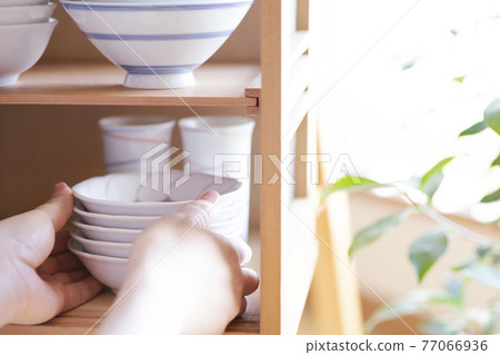 Female hand taking dishes out of the cupboard Female hand taking dishes out of the cupboard 77066936