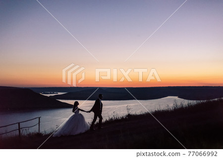 Silhouettes of bride and groom at night against lake and islands 77066992