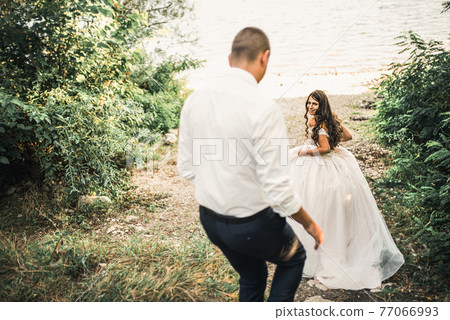 bride and groom laughing run together against rays of setting sun in summer  77066993